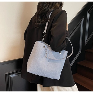 Detailed side view of a large light blue textured tote bag worn by a model in a modern space