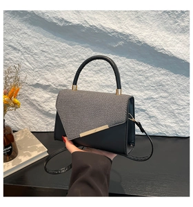 Détail du rabat en tissu gris et garniture dorée sur un sac à main noir minimaliste