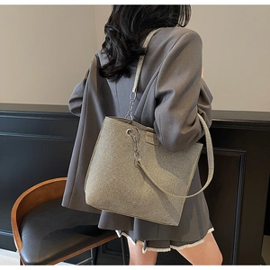 Macro side view of a large champagne gold textured tote bag with chain strap on model