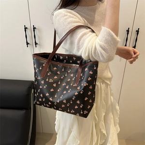 Grand sac cabas noir avec imprimé cerise rouge et anses marron porté par un modèle