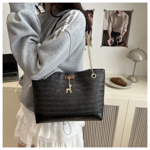 Detail of black woven tote bag with golden deer charm and leather base in a home setting
