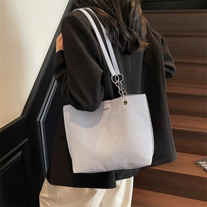 Light blue textured tote bag with chain strap detail shown on model in a modern interior