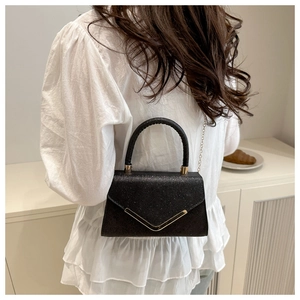Detail of black glitter crossbody bag with elegant gold V-shape buckle and chain strap
