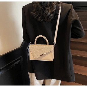 Petit sac carré beige à paillettes porté par un mannequin en blazer noir avec poignée nouée