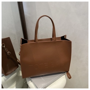 Detail of a brown matte leather tote bag featuring a minimalist embossed lettering design