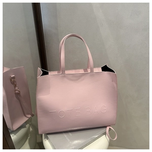 Detail of pink faux leather tote bag with embossed lettering and metal strap hooks