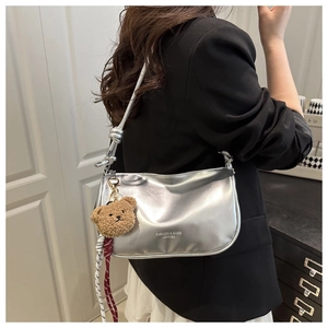 Detail of silver metallic crescent bag with knotted strap and small bear charm