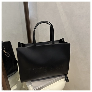 Detailed view of the embossed TOTE BAG lettering on a black matte leather tote bag