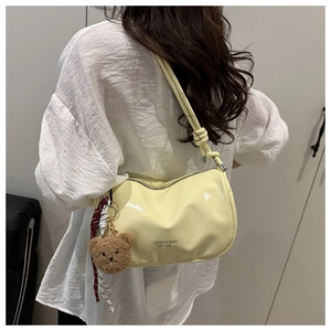 Detail of light yellow patent leather shoulder bag with plush bear charm and ribbon