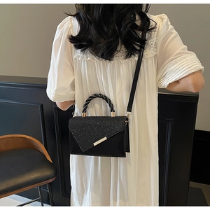 Détail d'un sac à main en cuir noir avec rabat scintillant et poignée torsadée bicolore