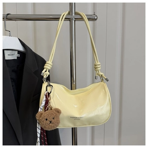 Detail of cream yellow leather pillow bag with knotted strap and brown plush bear charm