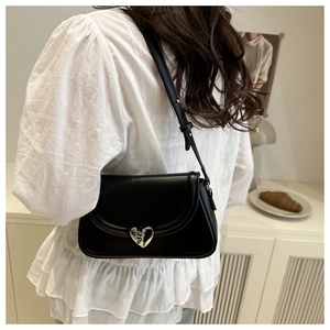 Détail d'un sac bandoulière en cuir noir avec une boucle métallique en forme de cœur