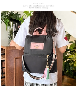 Detail of black nylon backpack featuring pink logo patch and colorful tassel charm