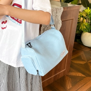 Minimalist light blue canvas crossbody bag shown on model with adjustable strap