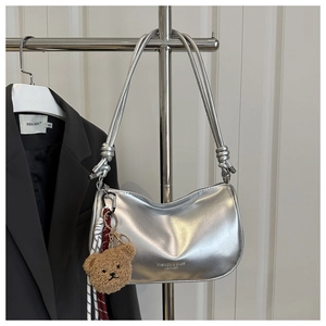 Detail of silver pillow bag with knotted strap and cute brown plush bear charm