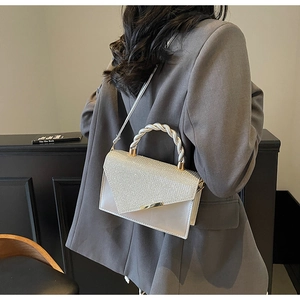 Détail d'un sac bandoulière blanc avec rabat pailleté et poignée métallique torsadée