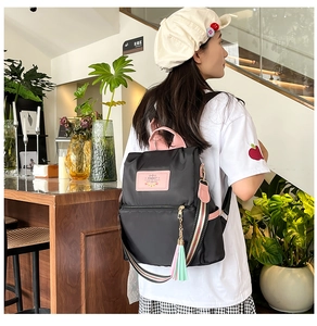 Close-up of black nylon backpack with pink details and colorful woven straps in a cafe