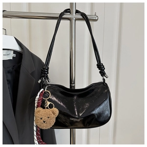Detail of glossy black pillow bag featuring a plush bear charm and fashion text logo