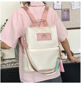 Detail of a creamy white nylon backpack with pink straps and decorative tassel hanging