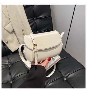 Detail of a creamy white saddle bag with adjustable leather strap and metal hardware
