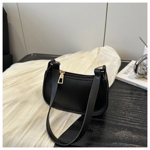 Detail of black litchi grain leather shoulder bag with gold hardware on wooden table