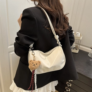 Minimalist cream white patent leather pillow bag with a plush bear charm worn by a model