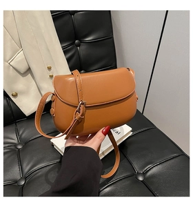 Close-up of a brown orange saddle bag made of smooth matte leather with a thin shoulder strap