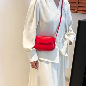 Minimalist red leather crossbody bag worn with elegant white silk outfit