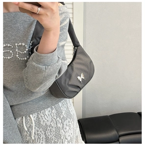 Detail of grey pleated crescent hobo bag with silver butterfly charm on a shoulder