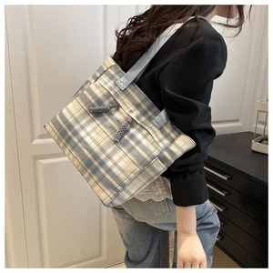 Detail of yellow and grey plaid tote bag featuring decorative woven knots and blue strap