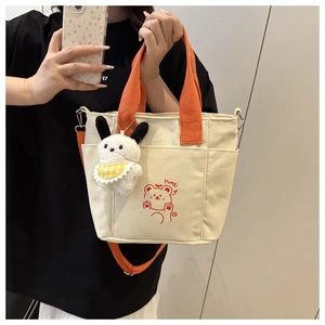 Detail of beige canvas tote with orange straps, cute bear print and plush dog charm