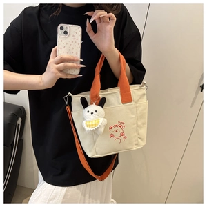 Detail of canvas bag with orange straps, side pockets and a cute plush bear charm