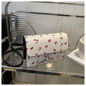 Détail du sac à bandoulière carré blanc avec imprimés cerises et breloque dorée
