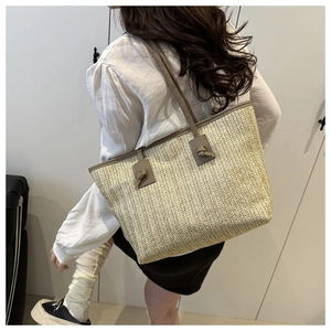 Detail of a large straw tote bag with brown leather straps shown on a model