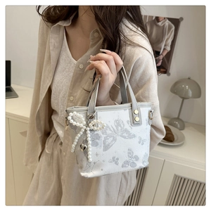 Detailed close-up of white bucket bag with butterfly print and pearl bow pendant