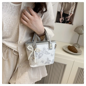Detail of white bucket bag with gray butterfly print and decorative pearl bow charm