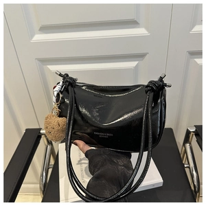 Détail d'un sac hobo en cuir verni noir avec sangle nouée et breloque ours