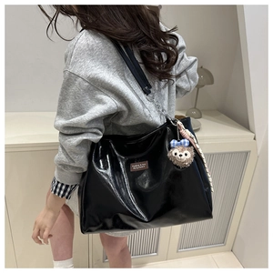 Detail of black patent leather tote bag with silver chain and plush charm accessory