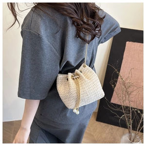 Detail of beige woven bucket bag featuring pearl drawstring and gold chain strap