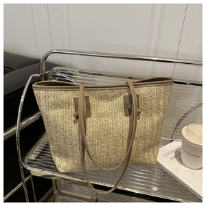 Detail of hand-woven straw tote bag with brown leather handles on a minimalist metal rack