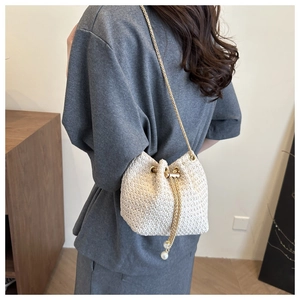 White woven bucket bag with pearl drawstring tassels and a gold chain strap worn by model