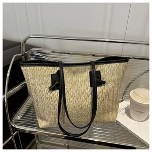 Detail of handwoven straw tote bag with black leather straps on a stylish shelf