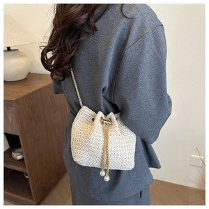 Detail of woven bucket bag with gold chain strap and elegant pearl drawstring accents