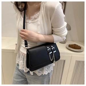 Close-up of black crossbody bag with silver buckles and chain on a stylish model