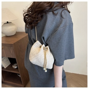 Detail of white woven bucket bag with elegant pearl drawstring and gold chain strap