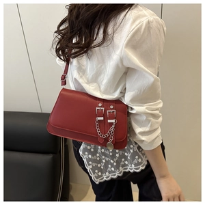 Detailed view of red leather shoulder bag with silver chain and dual buckle design