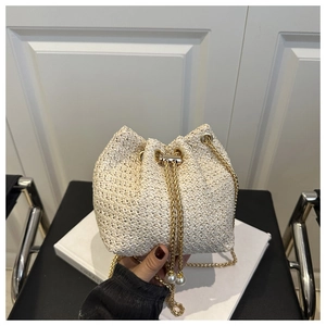 Detail of straw bucket bag featuring a gold chain strap and pearl drawstring charms