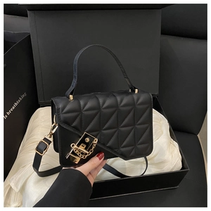 Close-up of black quilted shoulder bag with gold hardware inside a gift box