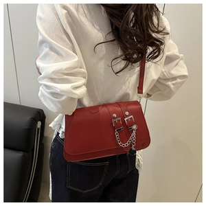 Detail of red crossbody bag with silver buckles and chain strap shown on a model