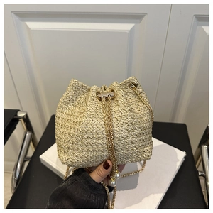 Detail of beige woven bucket bag with gold chain strap and elegant pearl drawstring charms